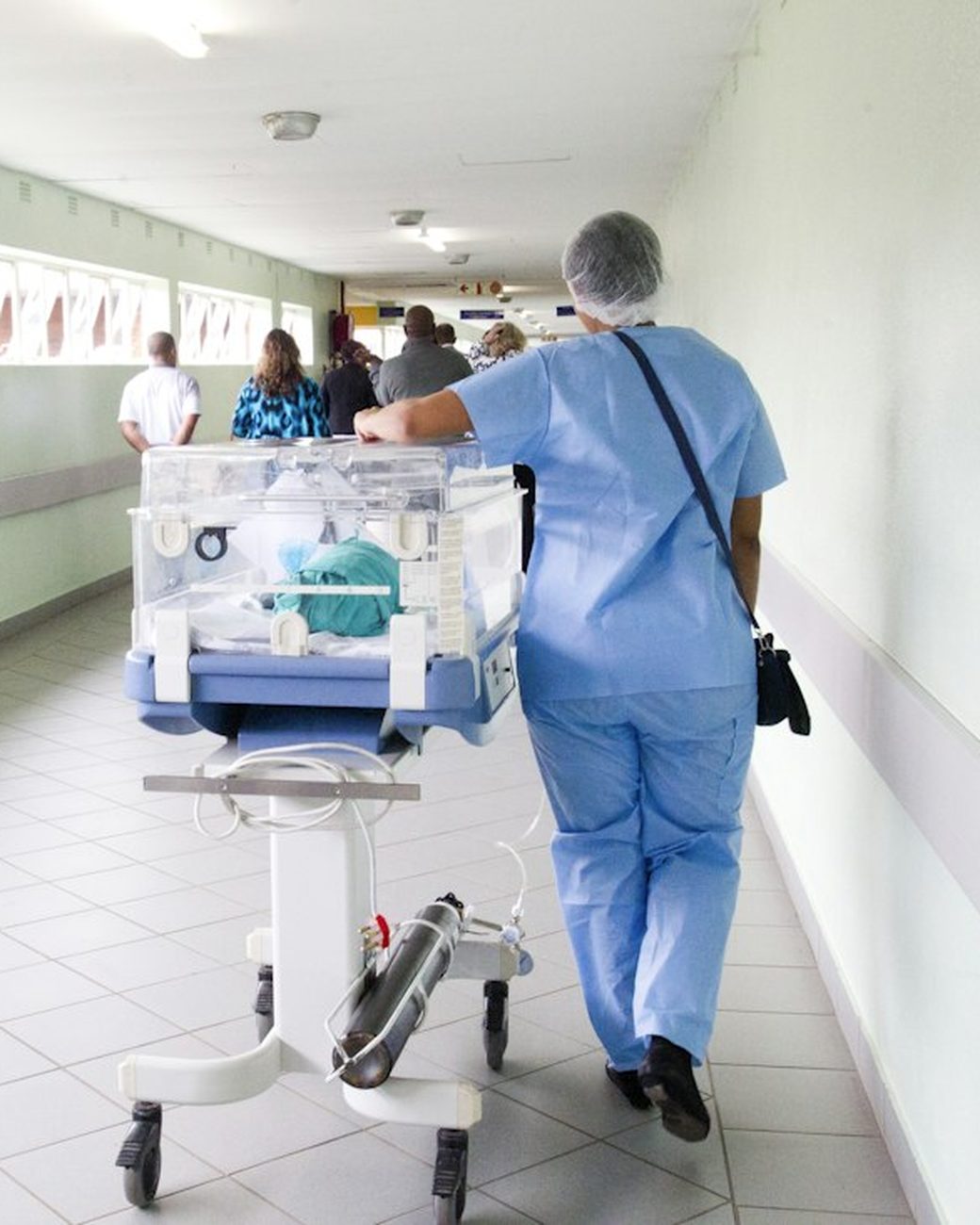 A nurse in scrubs pushing a hospital trolley down a corridor